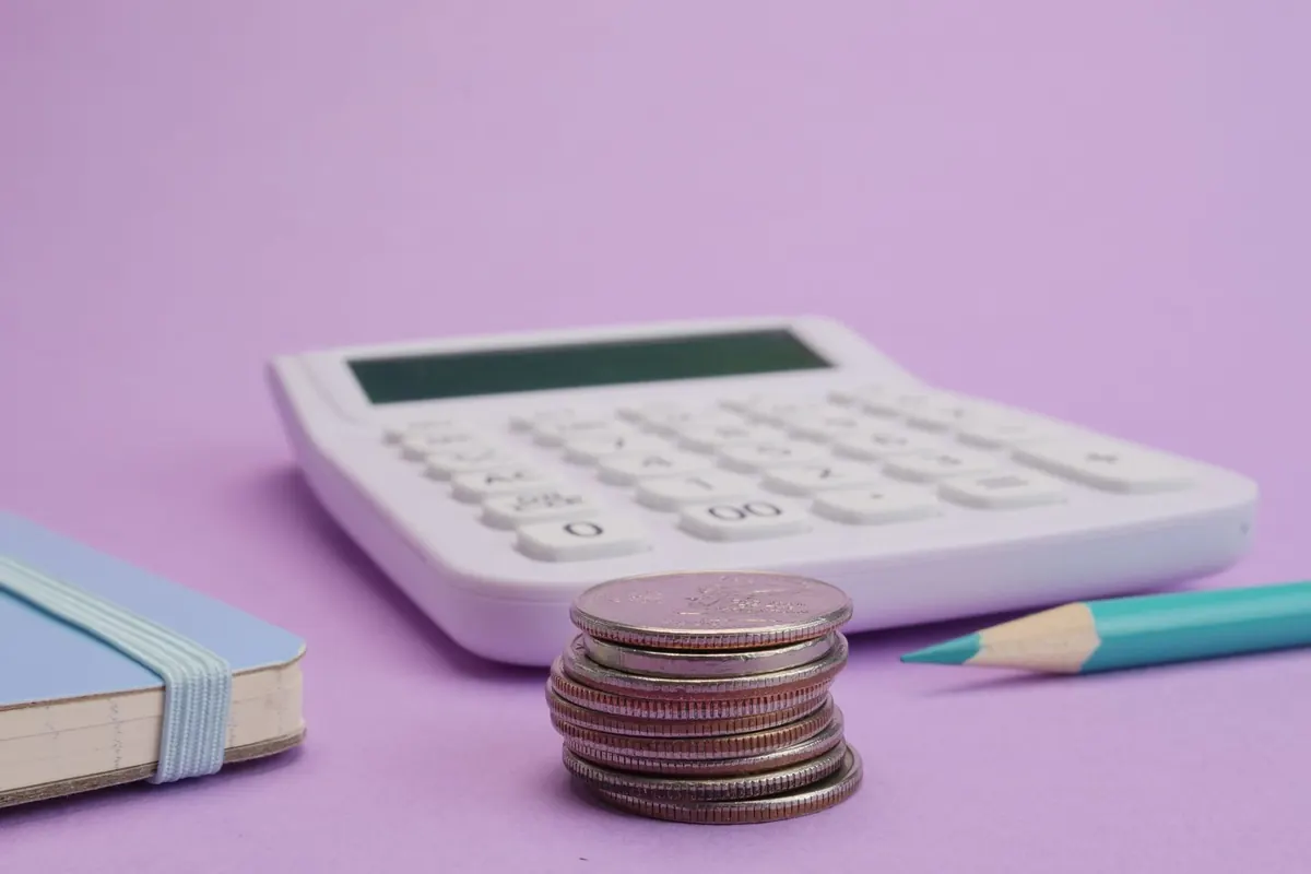 Calculatrice, pile de pièces et carnet posés sur un bureau