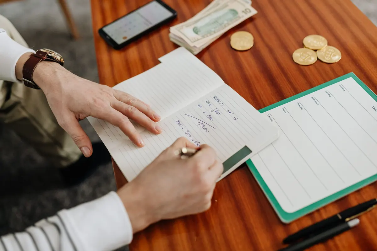 Personne qui note ses dépenses dans un carnet à côté de pièces et de billets