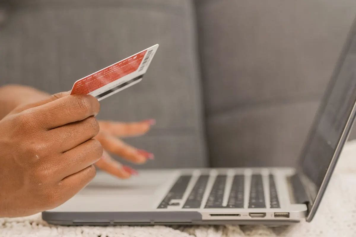 Main qui tient une carte bancaire devant un ordinateur portable