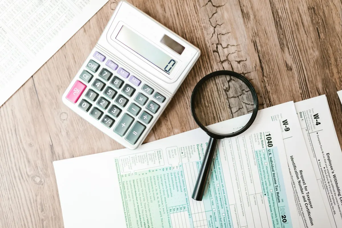 Calculatrice et loupe posées sur des formulaires fiscaux