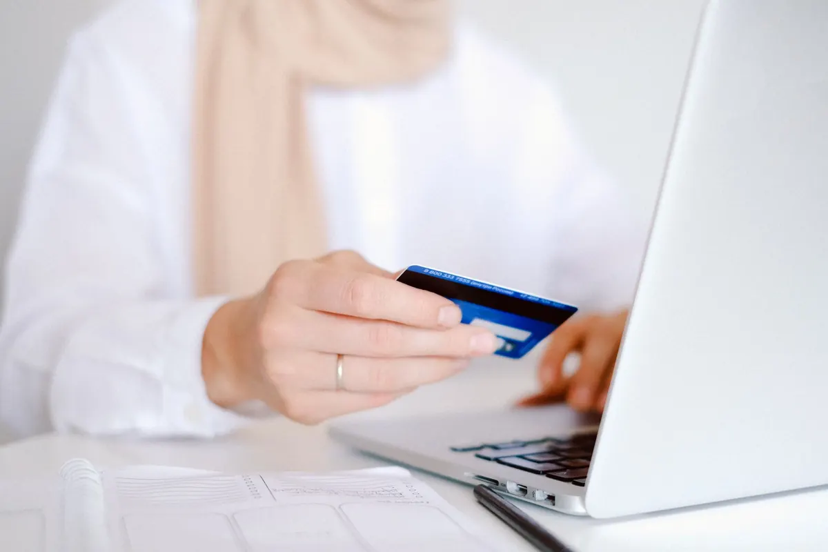 Femme qui tient une carte bancaire devant un ordinateur portable